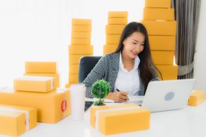 Portrait beautiful young asian business woman work from home with laptop mobile phone with cardboard box ready for shipping online shopping